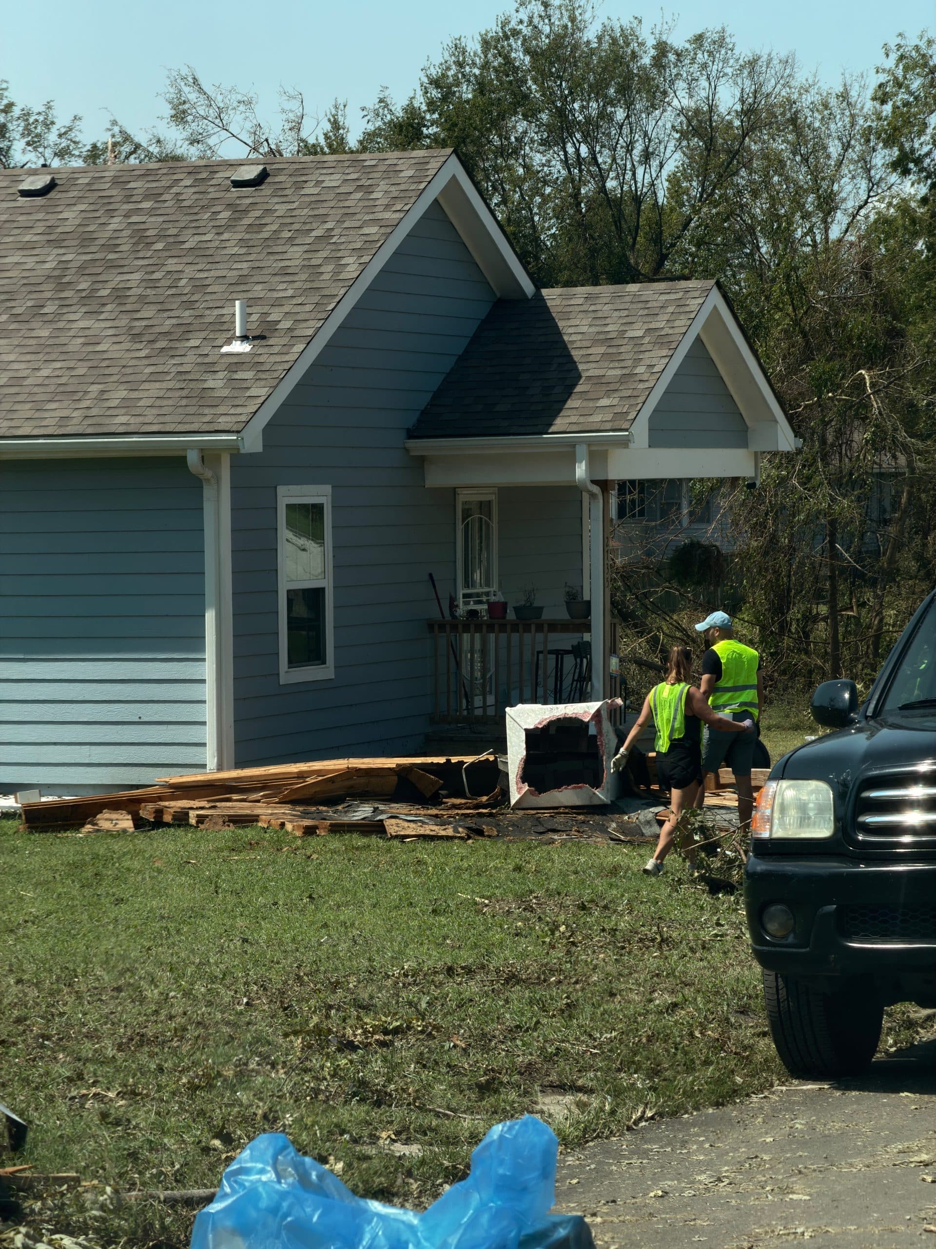 Neighbors clearing debris beside a damaged house