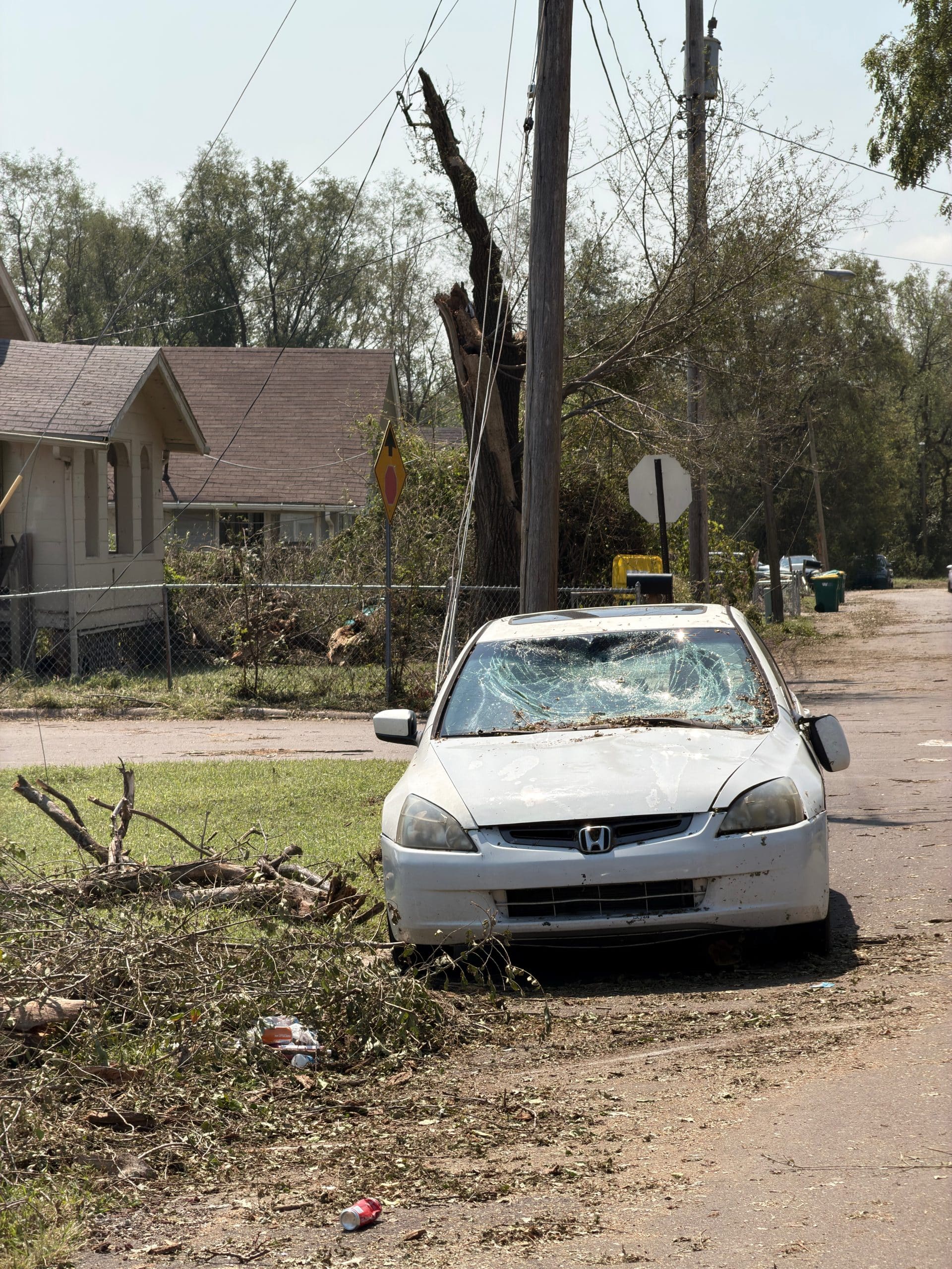 A damaged car beneath a leaning utility pole