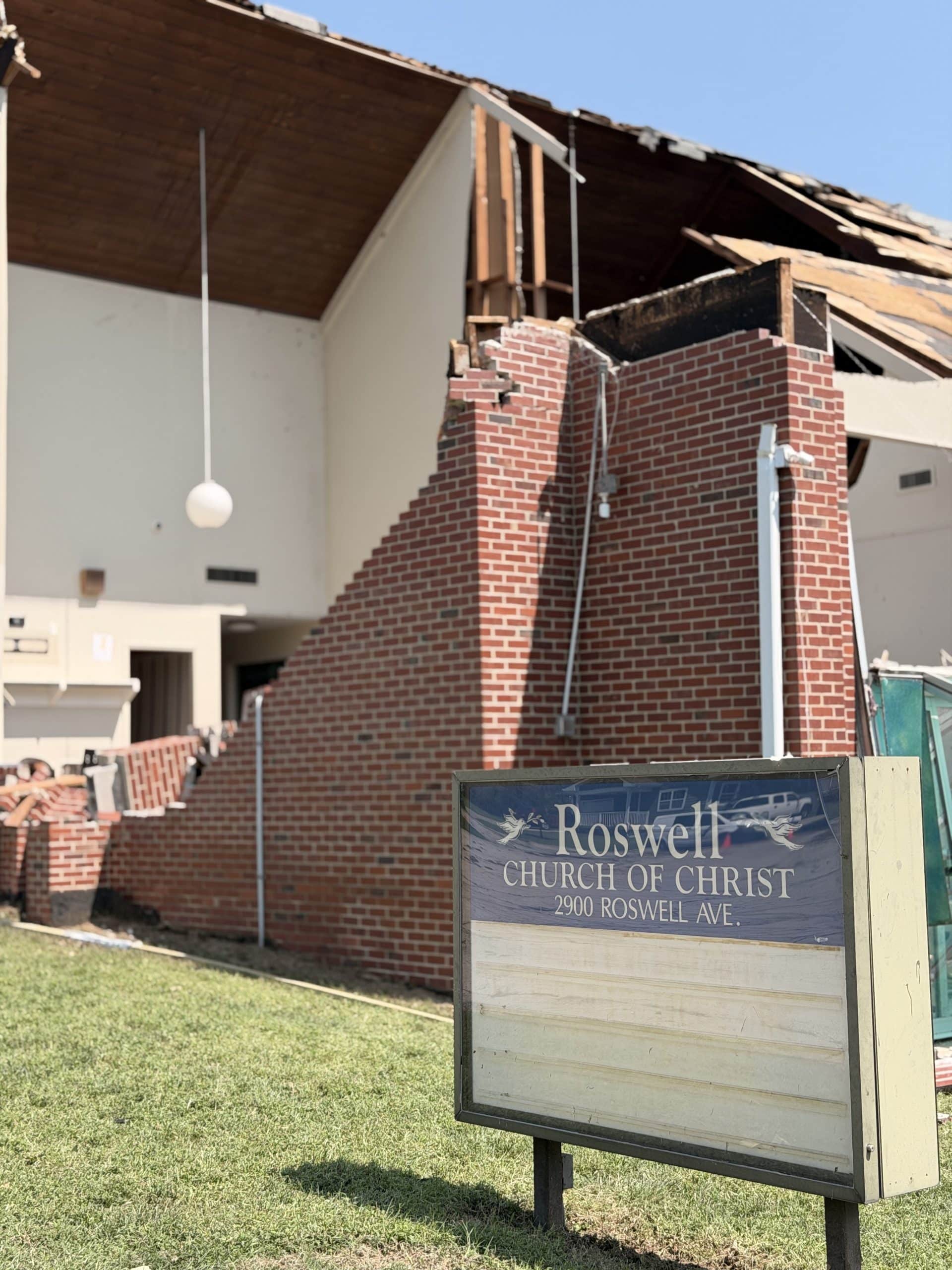 The Roswell Church of Christ sign standing before the sanctuary's collapsed brick wall and torn-open roof