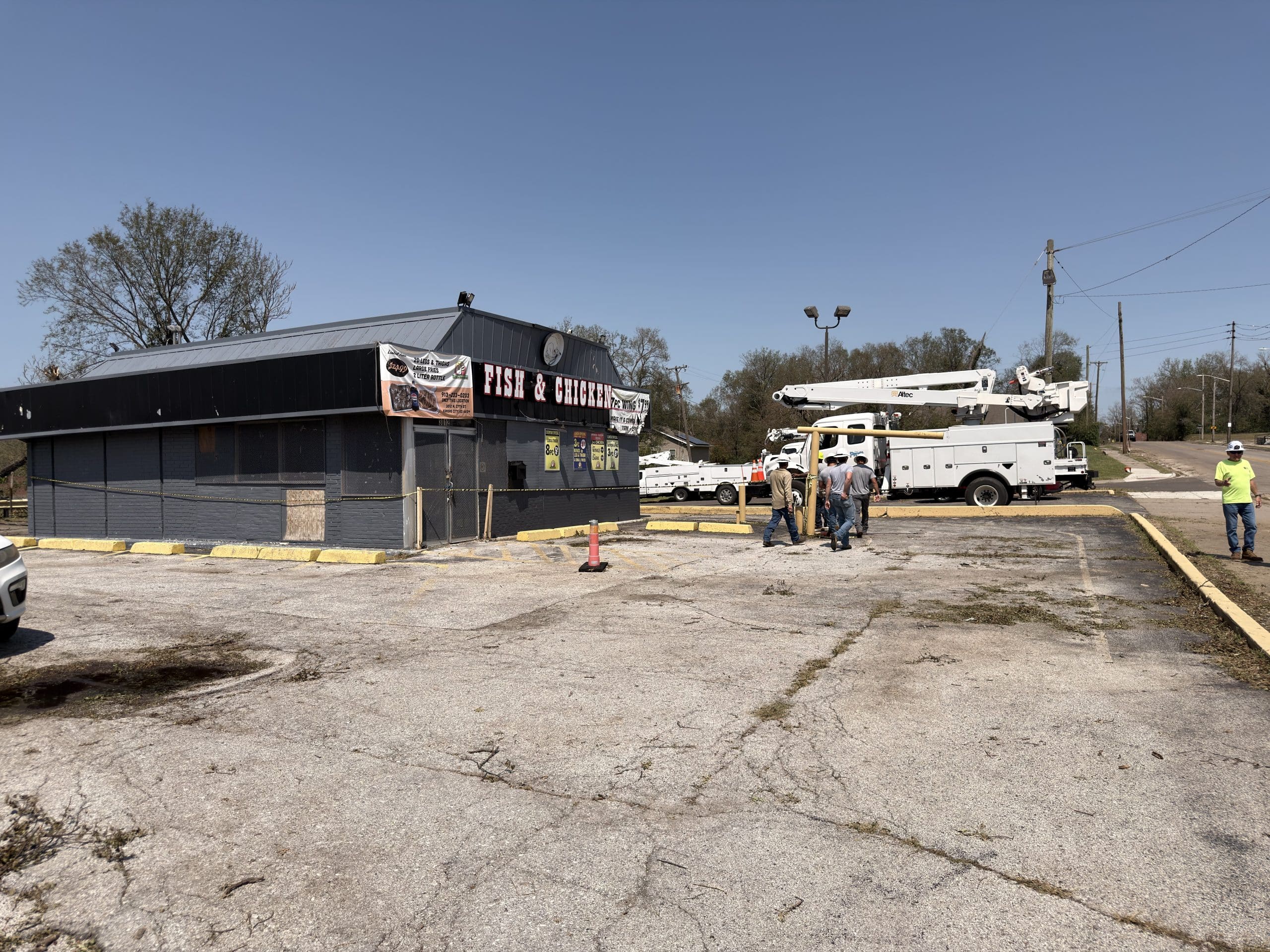 Utility trucks and crews staged in a lot beside a Fish and Chicken restaurant
