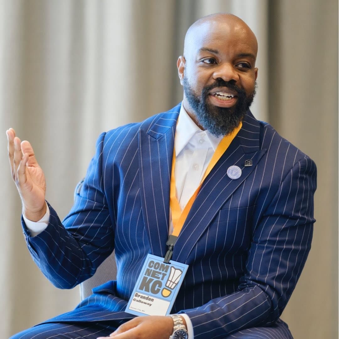 Brandon Calloway, in a navy pinstriped suit, gestures with one hand while speaking at an event.