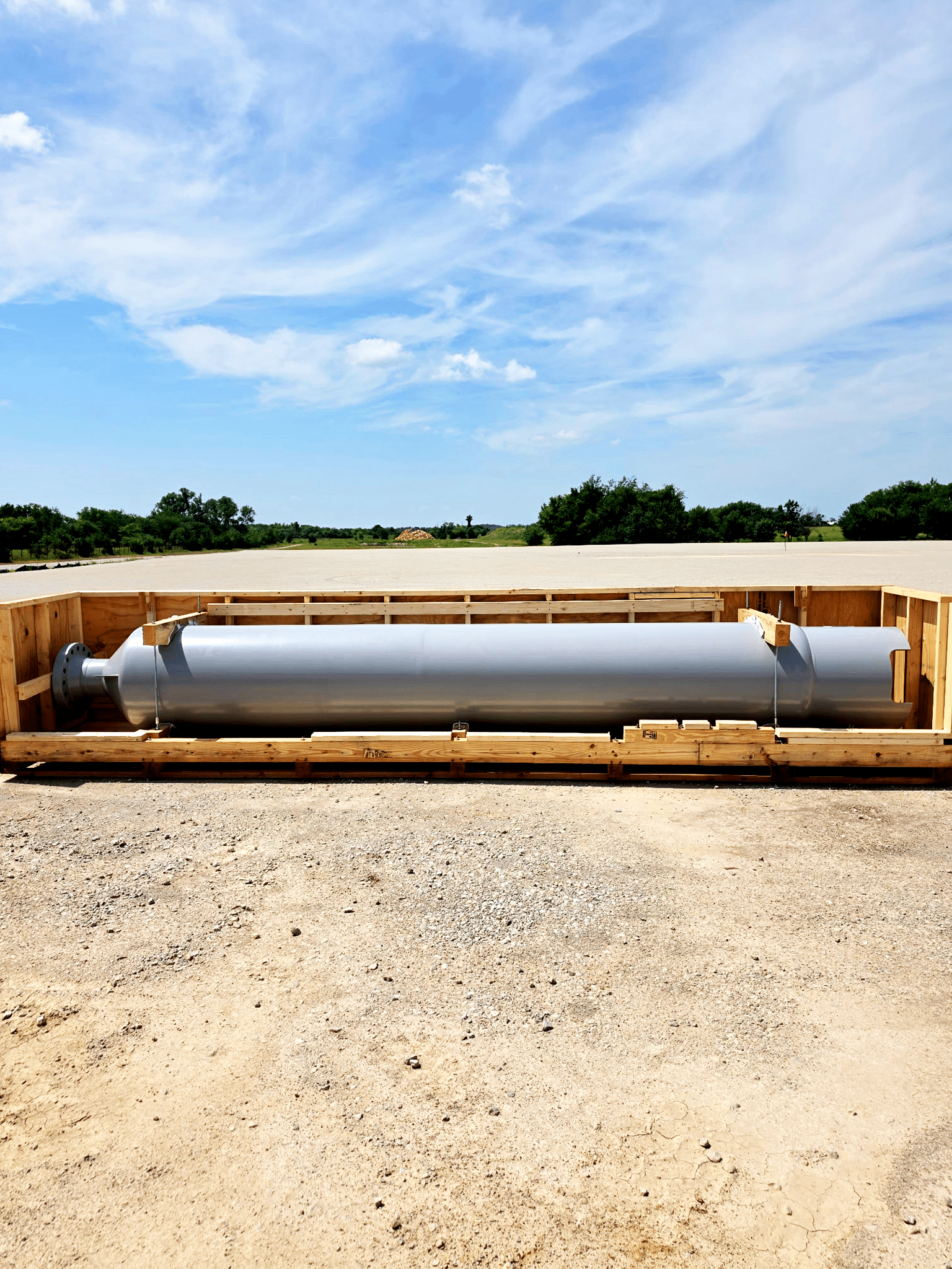 A reactor canister rests on supports in an open field.