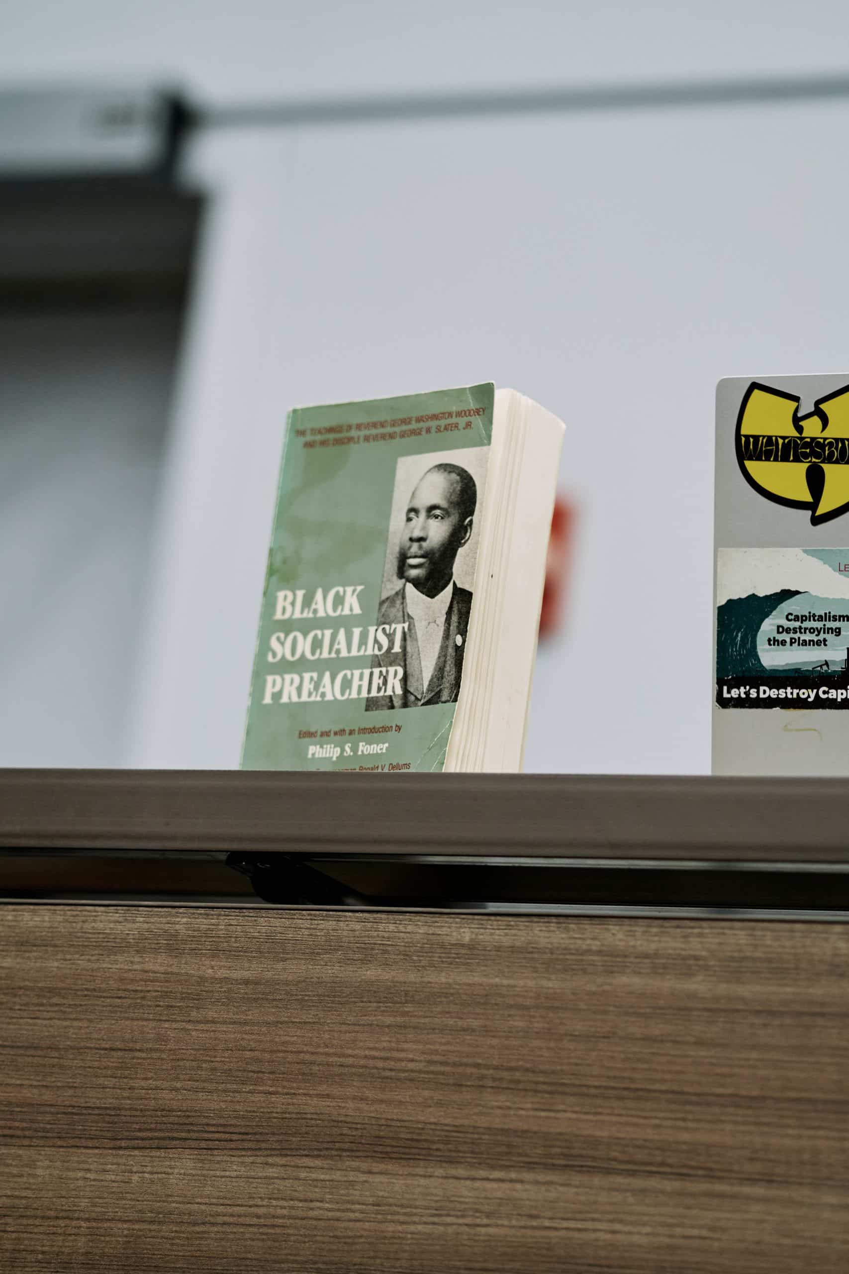 A worn paperback copy of Black Socialist Preacher, edited by Philip S. Foner, stands upright on a wooden table. The green cover carries a portrait of Rev. George Washington Woodbey.
